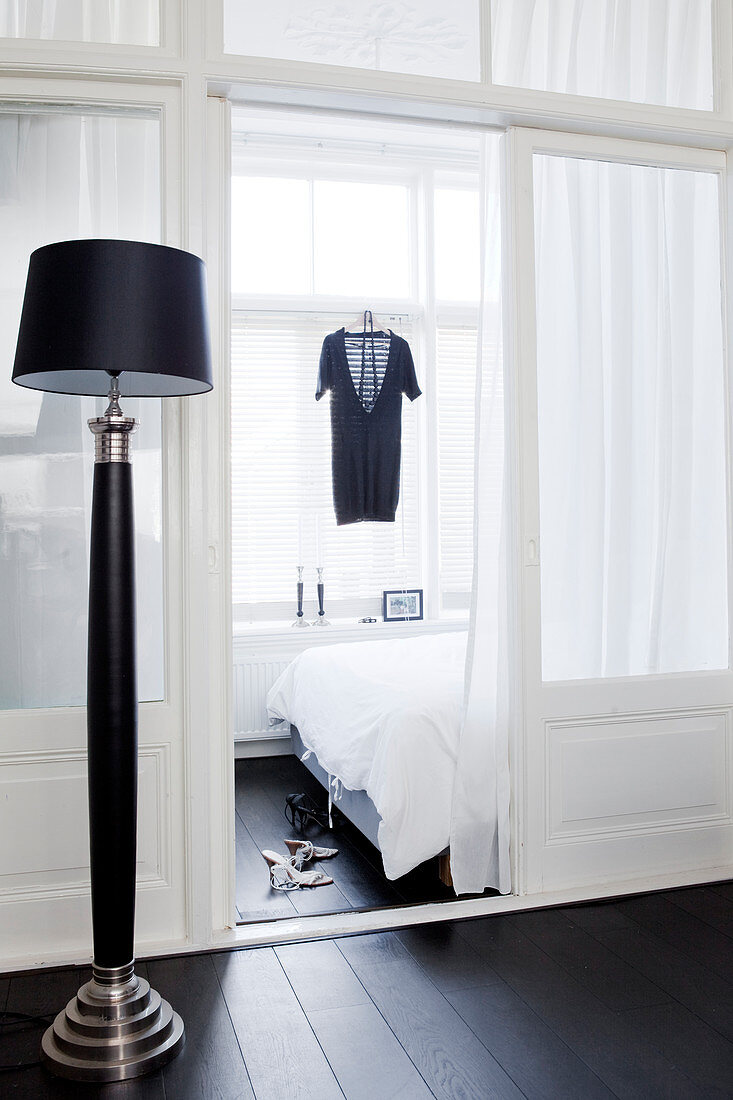 Black floor lamp in front of a glass room divider, with a view into the bedroom