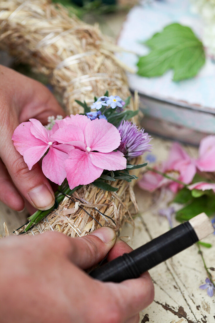 Tying hydrangea florets, forget-me-nots and chive flowers onto straw wreath