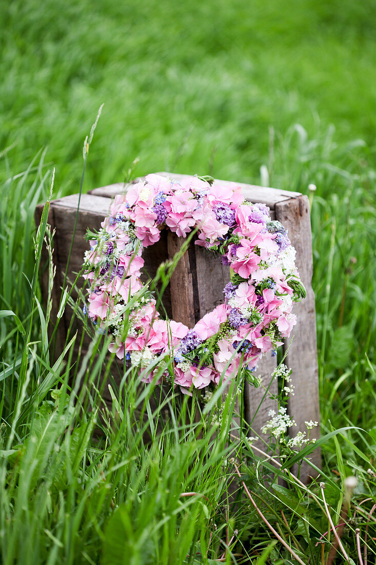 Wreath of hydrangea florets, forget-me-nots and chive flowers on wooden crate in meadow