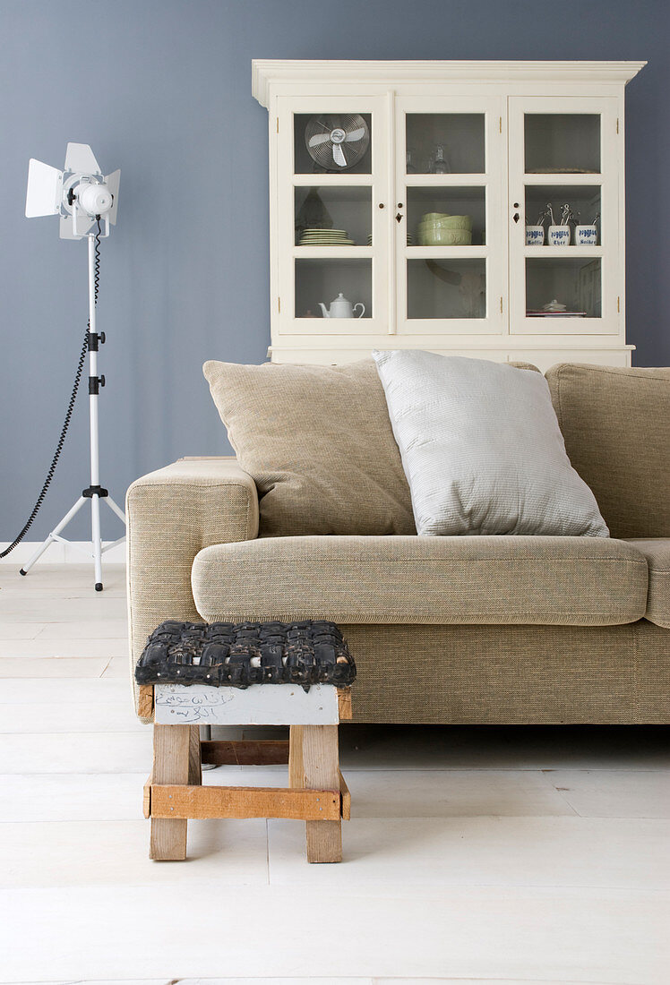 Recycling-Hocker vor beigem Sofa im Wohnzimmer mit blau-grauer Wand