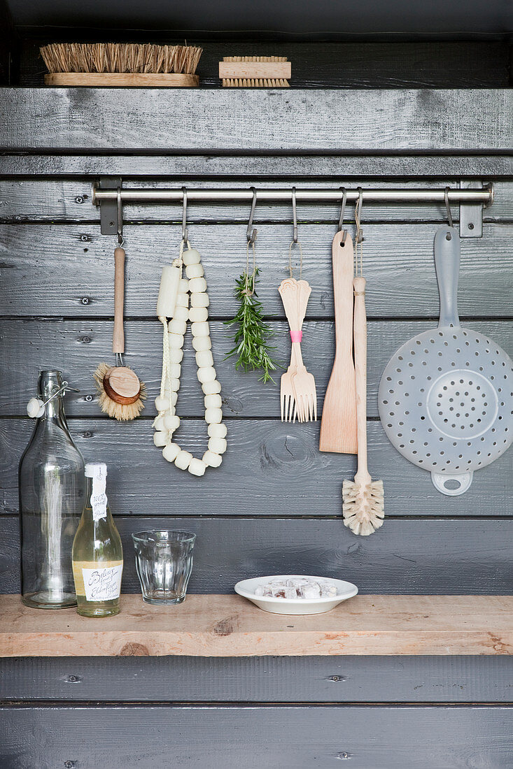 Kitchen utensils hanging from row of hooks on grey board wall