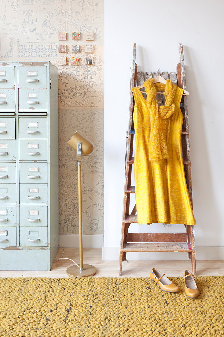 Gelbes Kleid hängt an einer Leiter neben hellblauem Schubladenschrank
