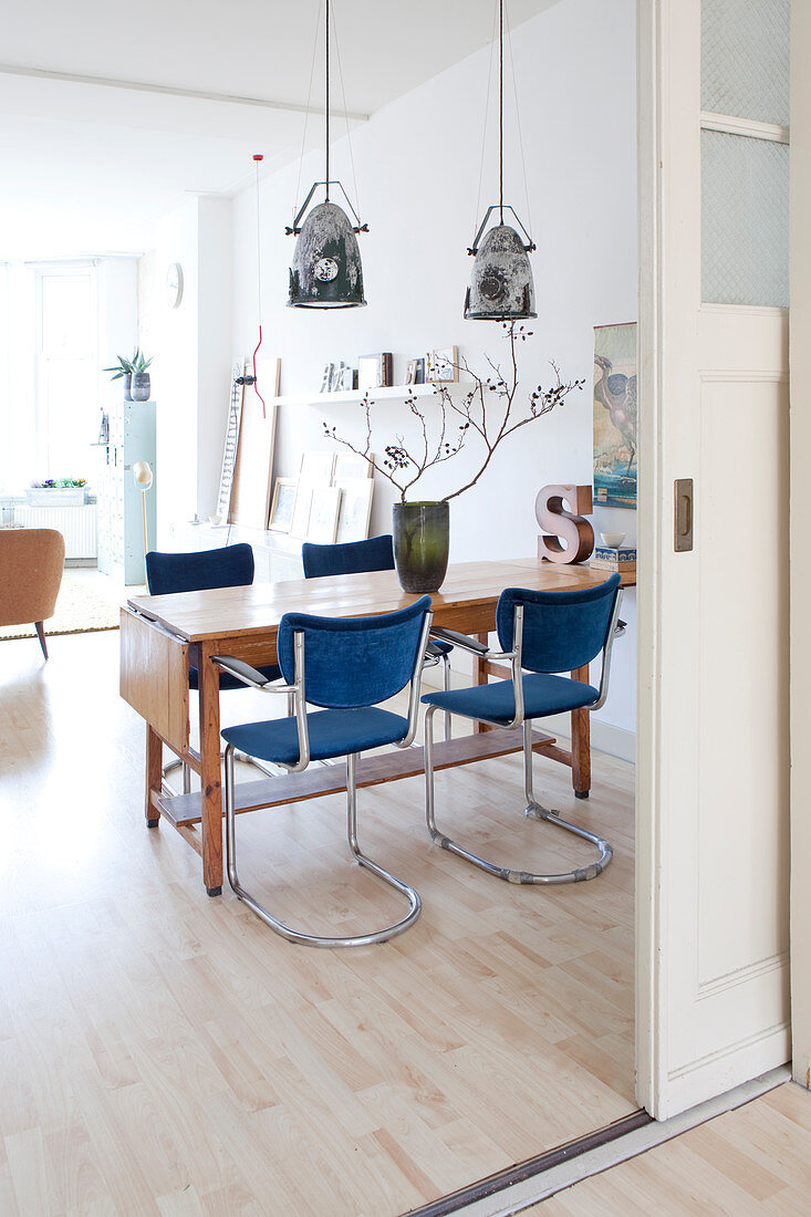 Esszimmer im Vintage-Stil mit blauen Schwingstühlen um alten Holztisch
