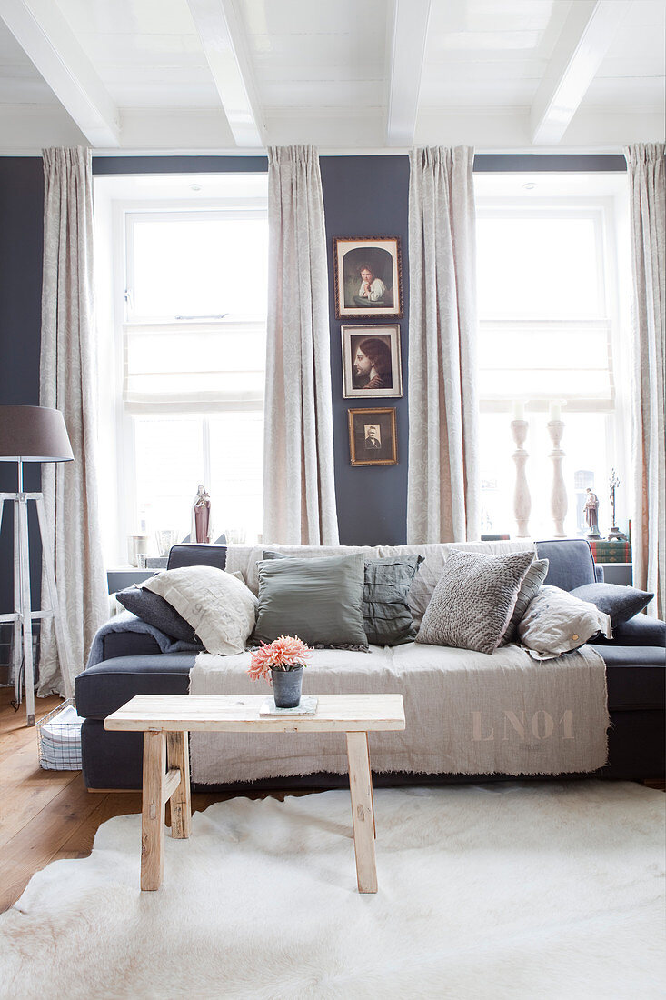 Sofa mit Kissen und Holzbank als Couchtisch im Wohnzimmer mit grauer Wand