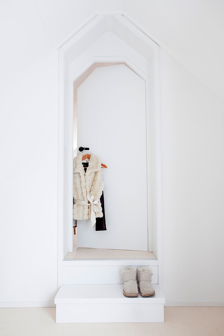 Weiße Tür mit Kleidungsstücken, davor Podest mit Schuhen