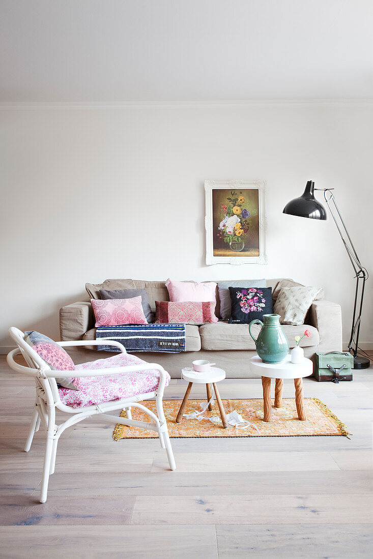 Sofa mit Kissensammlung und Rattanstuhl im Wohnzimmer in Pastelltönen