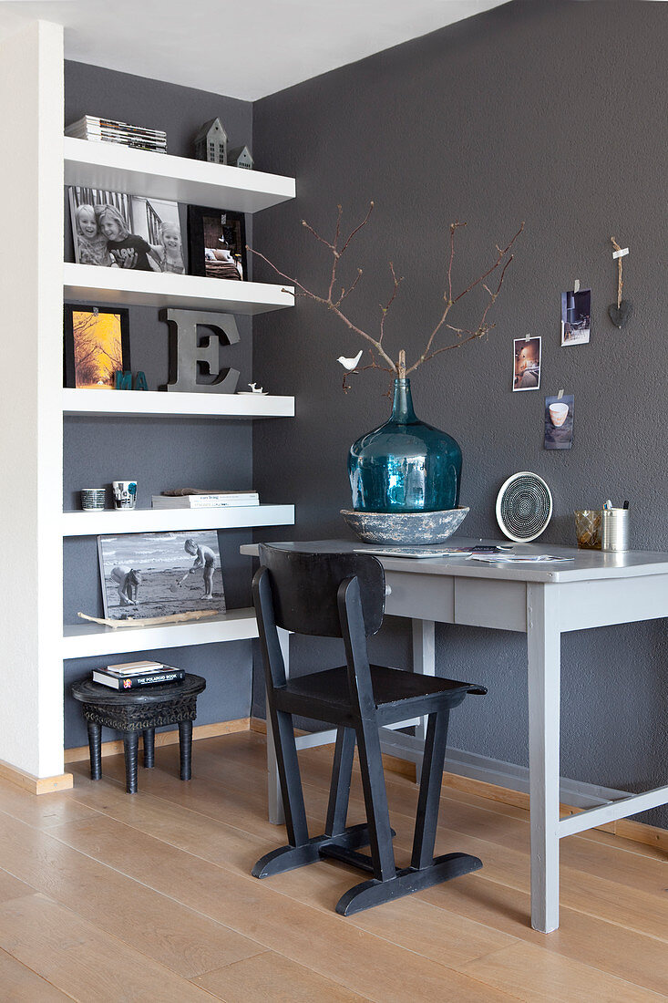 Schreibtisch mit Stuhl und Wandregal im Arbeitszimmer mit dunklen Wänden