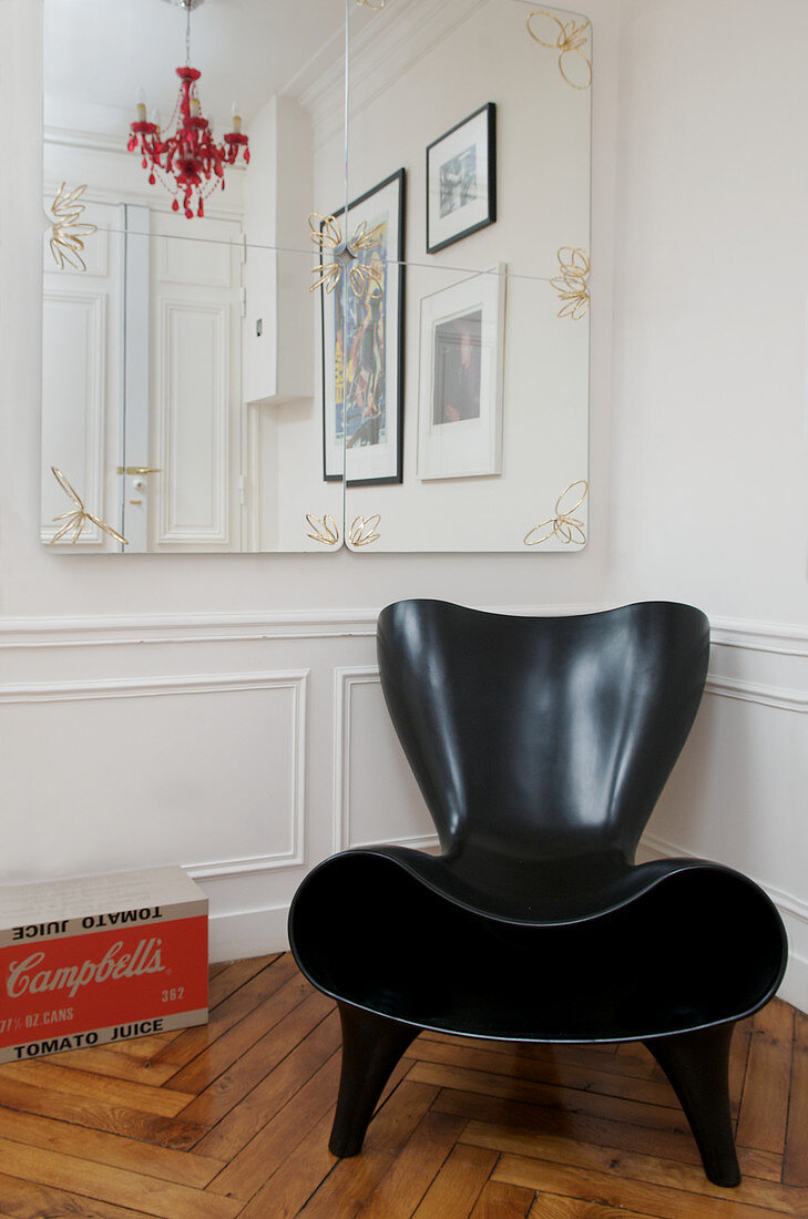 Moderner schwarzer Designersessel vor Wand mit Kassettenverkleidung und Spiegeln