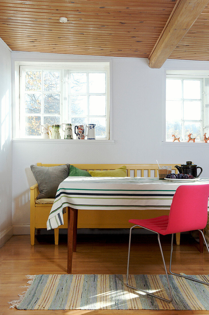 Striped tablecloth on table, pink chair and yellow bench in dining room