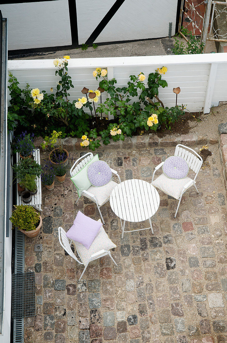 View down into paved courtyard with seating area and rose bed