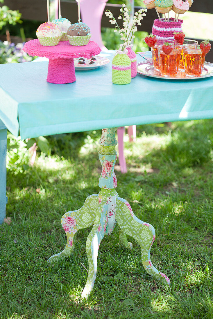 Old table with colourful fabric decoupage anc crocheted accessories in garden