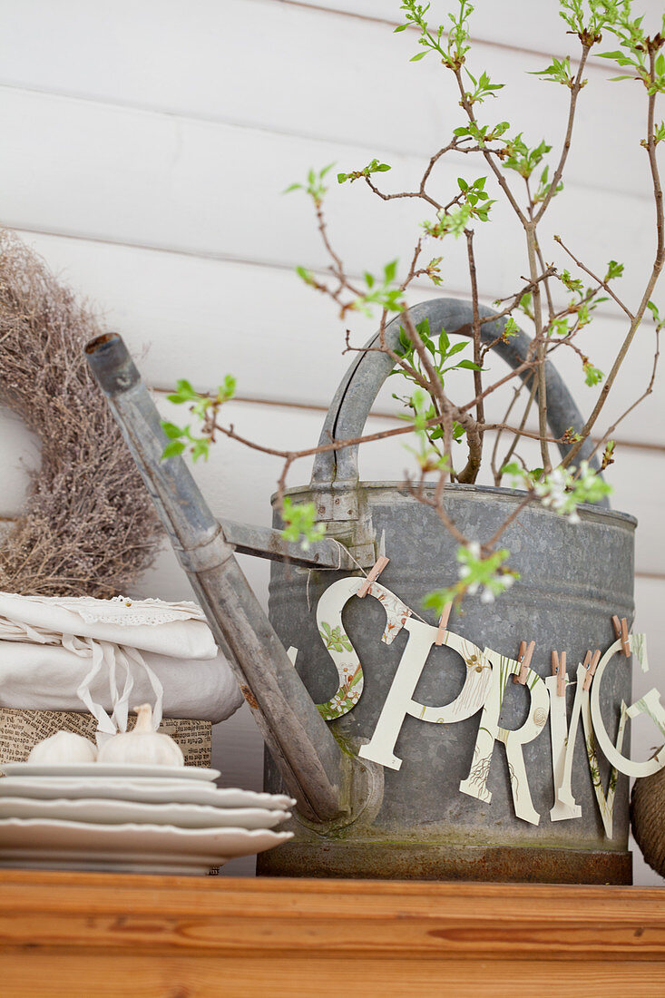 Garland of paper letters spelling 'Spring' on metal watering can of twigs