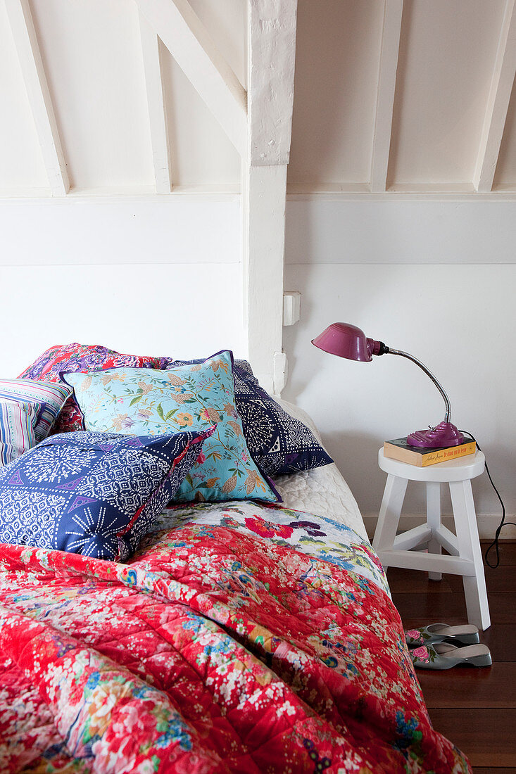 Bett mit bunten Kissen und Steppdecke in weißem Dachgeschosszimmer