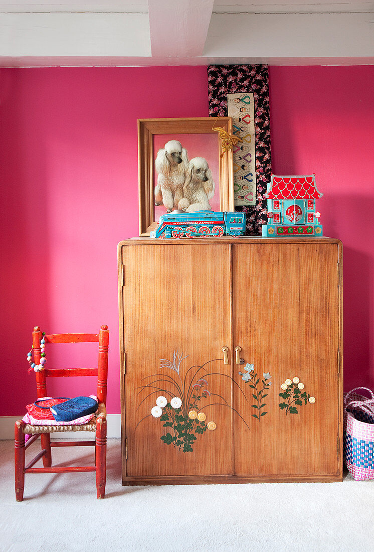 Alter Holzschrank mit Blumenmotiv vor pinkfarbener Wand im Mädchenzimmer