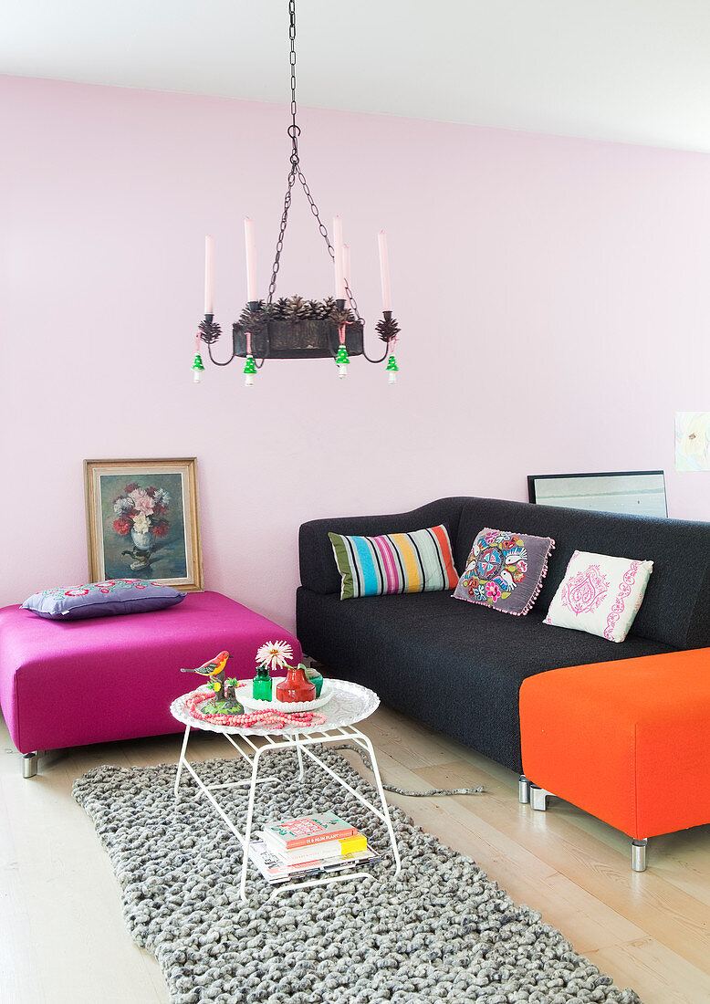 Sofa and brightly coloured ottomans in living room with pale pink wall