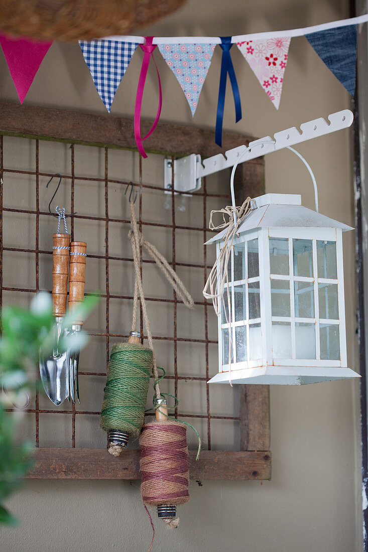 Lantern, twine and gardening tools hung on metal grid and string of bunting