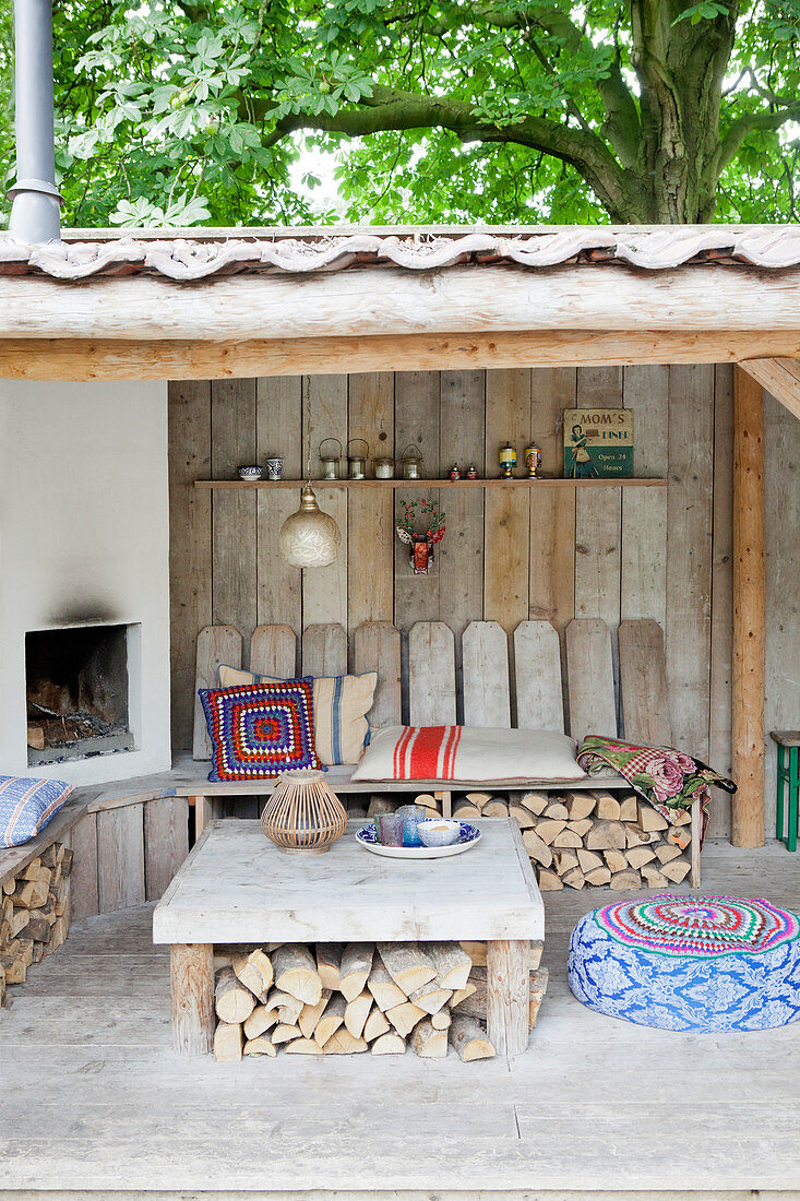 Fireplace with bench and table on a covered terrace with a wooden wall