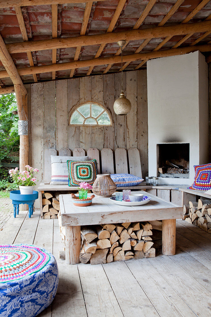 Kamin mit Sitzbank und Tisch auf überdachter Terrasse mit Bretterwand