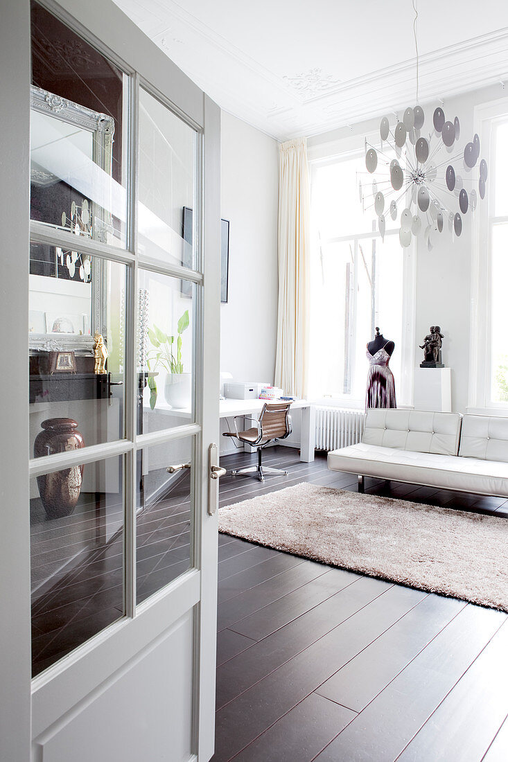 Blick durch geöffnete Tür auf weiße Ledercouch und Schneiderpuppe in Loft-Wohnung