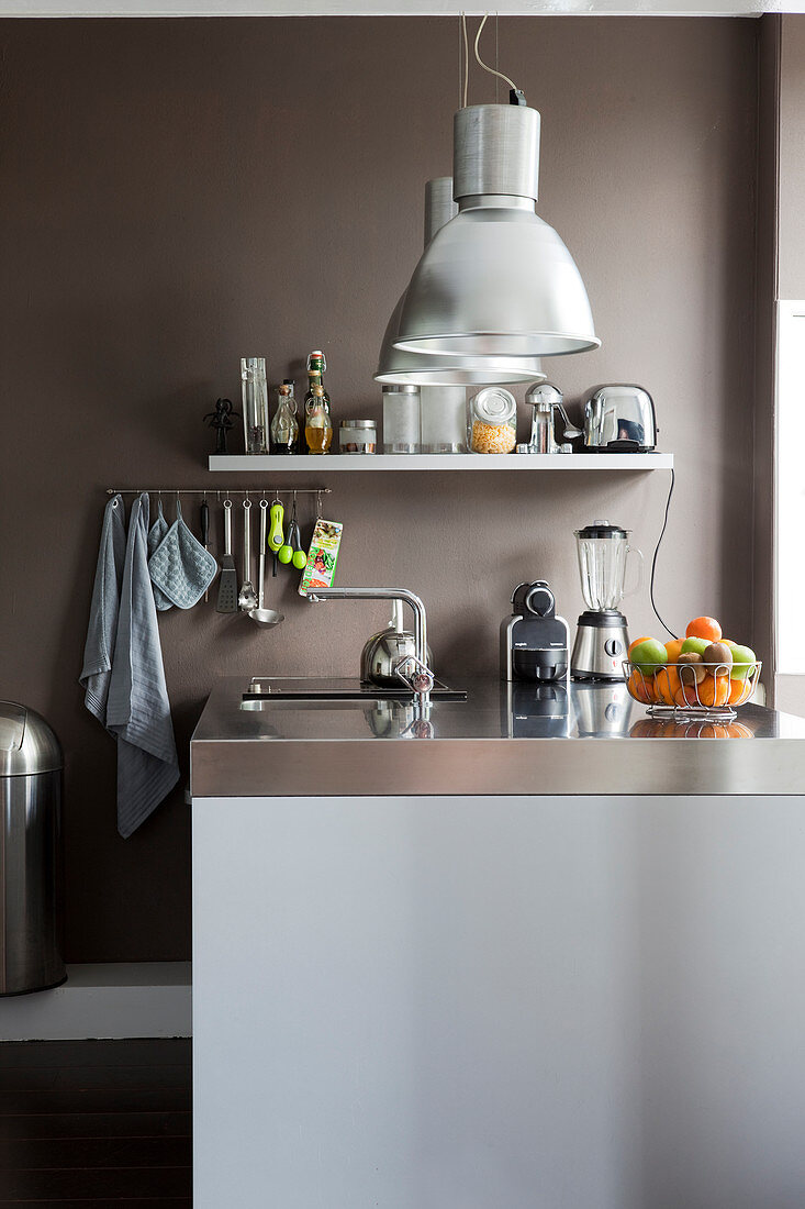 Küchentheke mit Edelstahl Arbeitsplatte, darüber Pendelleuchten in Küche mit brauner Wand