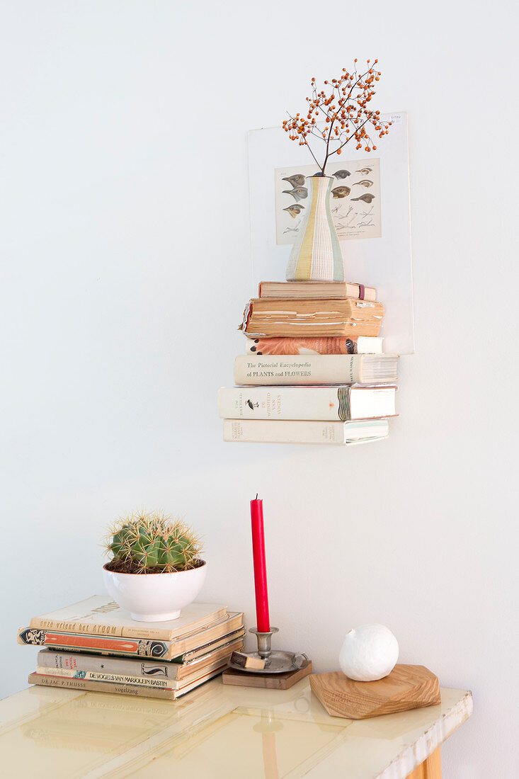 Books and vase on small shelf above candle, books and cactus on table
