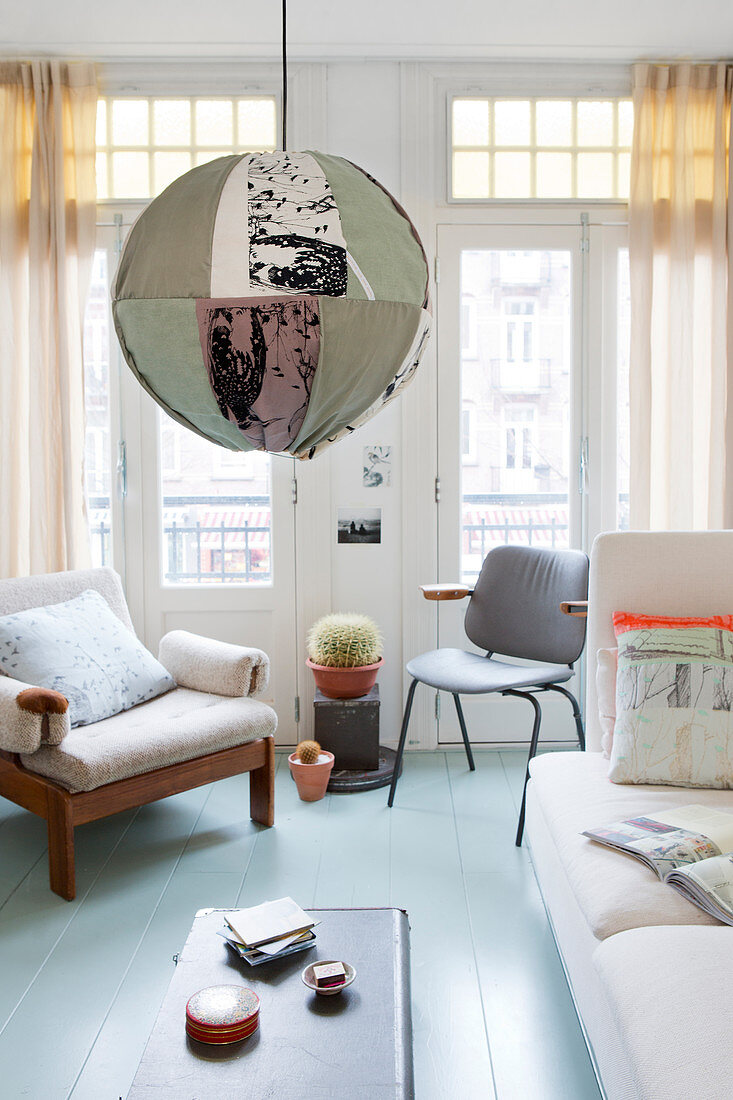 Kugelleuchte mit buntem Stoffschirm, helles Sofa, Stuhl und Sessel im Altbau-Wohnzimmer