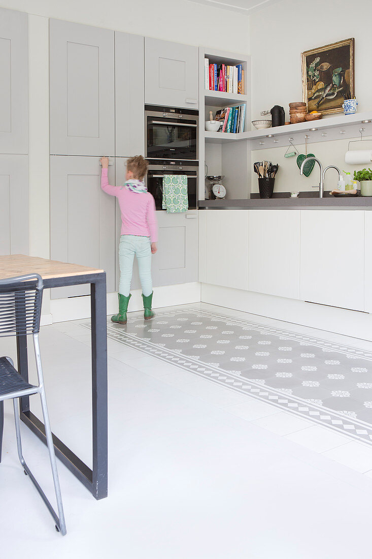 Girl standing in front of grey cupboards in kitchen with pattern painted on floor