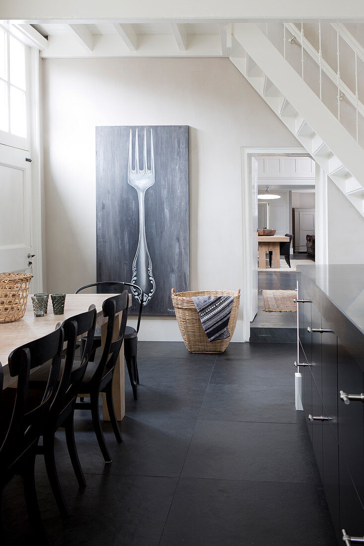 Schwarze Stühle am Esstisch vorm Bild mit Gabel-Motiv in der Wohnküche