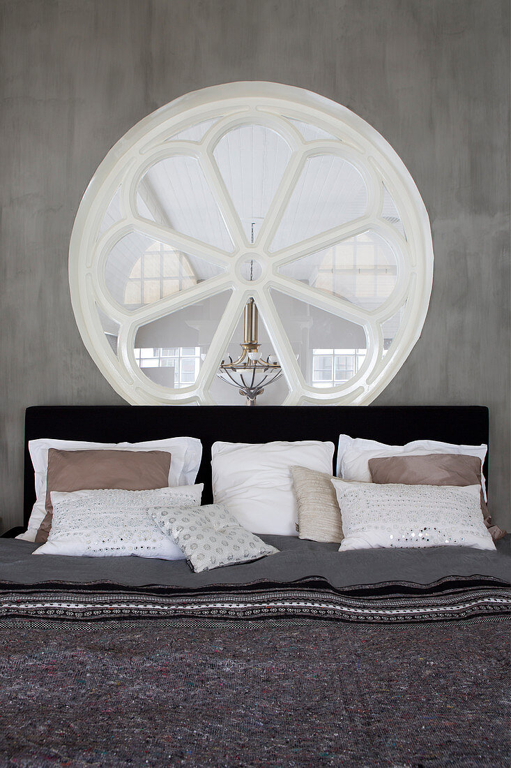 Bett unterm runden Sprossenfenster in grauer Wand