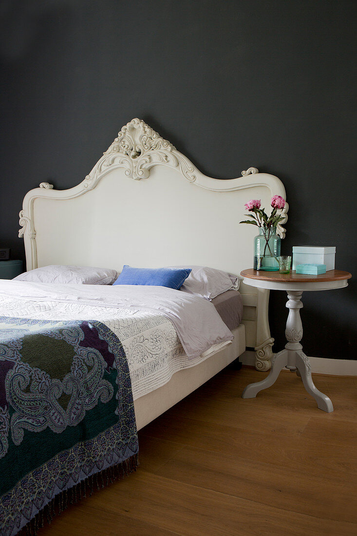 Bett mit barockem Betthaupt und Balustertisch vor schwarzer Wand