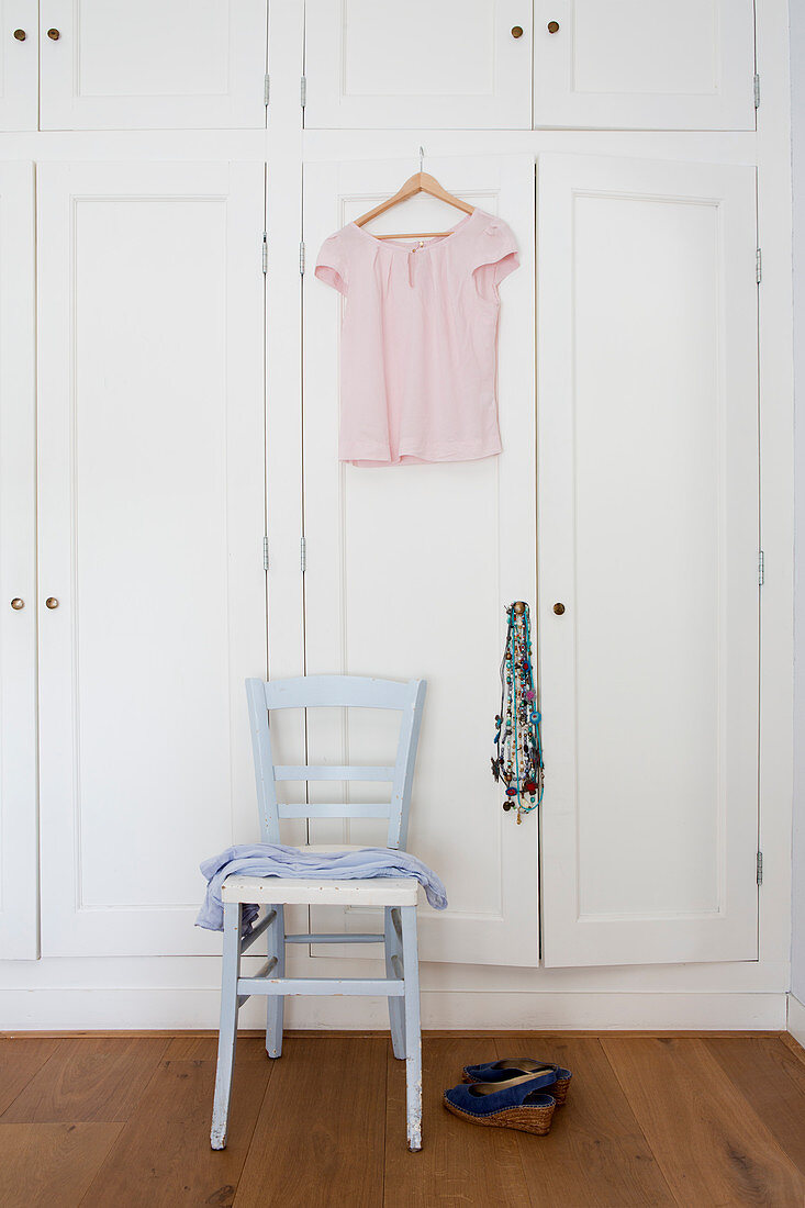Rosafarbene Bluse hängt am Schrank über hellblauem Stuhl