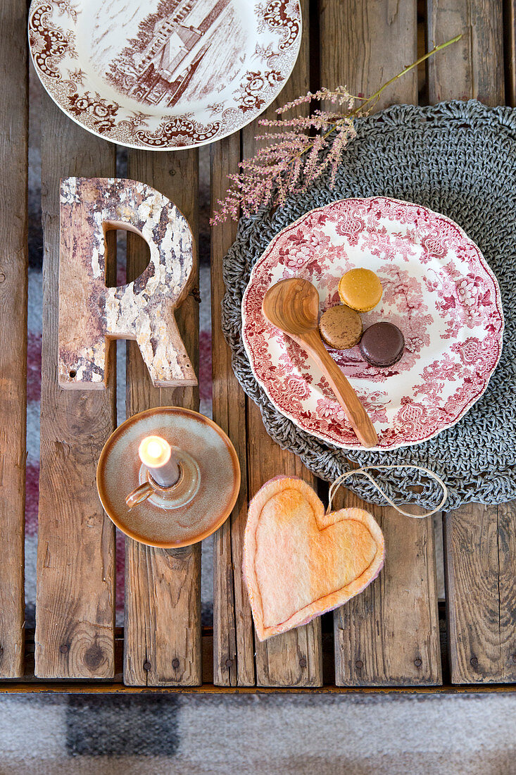 Country-house plates, decorative letter, heart-shaped pendant and candle on rustic wooden table