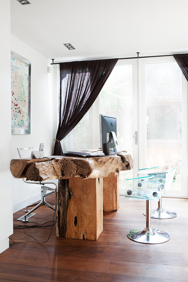 Transparente Schalenstühle vorm rustikalen Schreibtisch aus massivem Holz