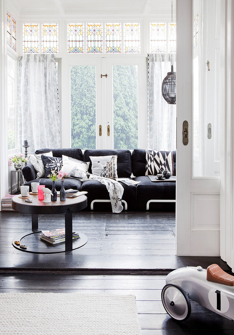 Blick ins Wohnzimmer mit schwarzem Sofa und Couchtisch vor Fenster
