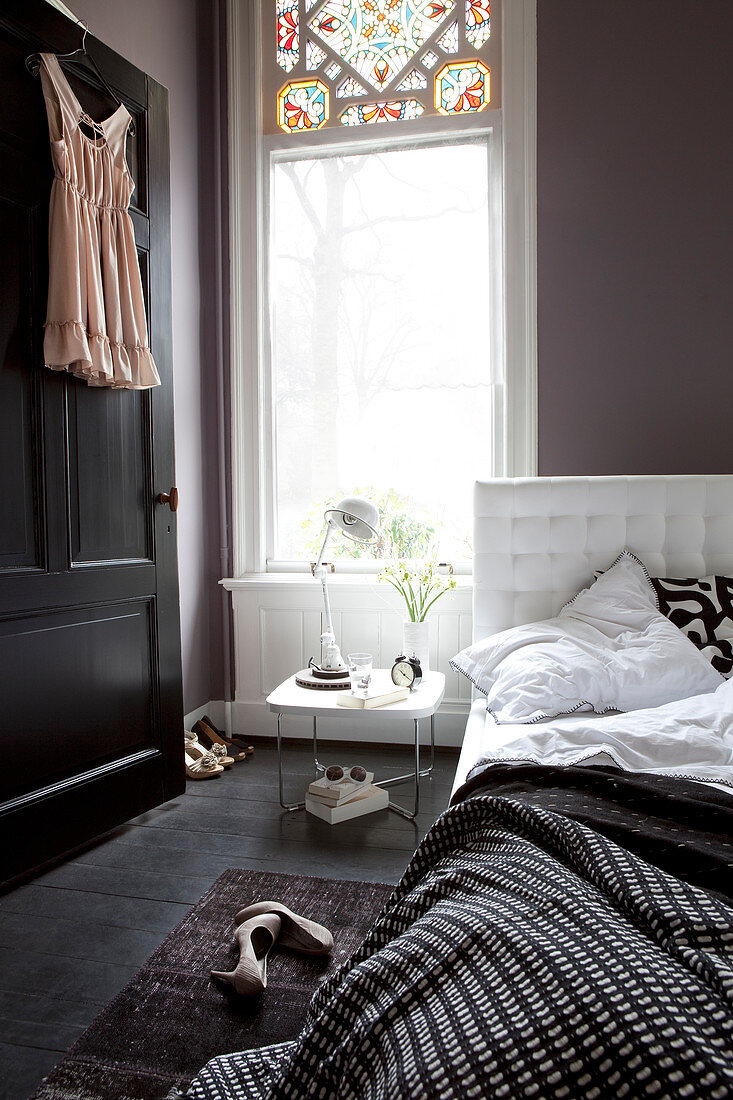 Bett mit schwarz-weißer Bettwäsche, Damenwäsche an schwarzer Tür im Schlafzimmer mit dunkler Wand