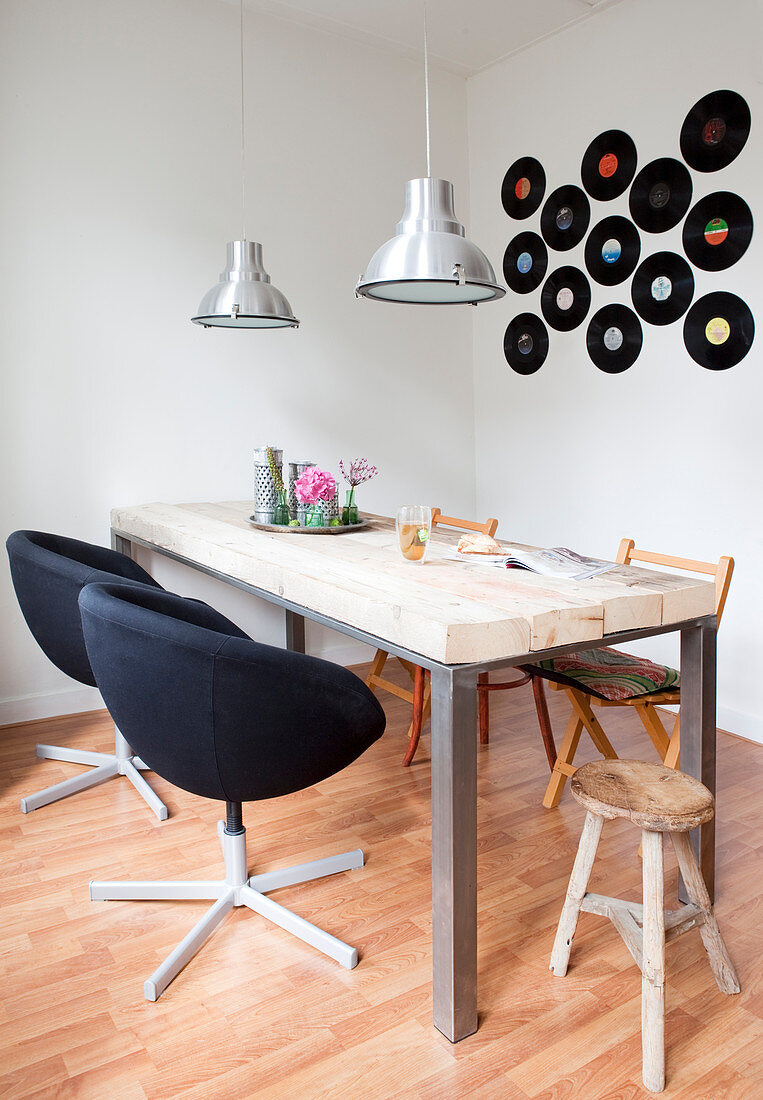 Arrangement of vinyl records on wall above dining table with various chairs