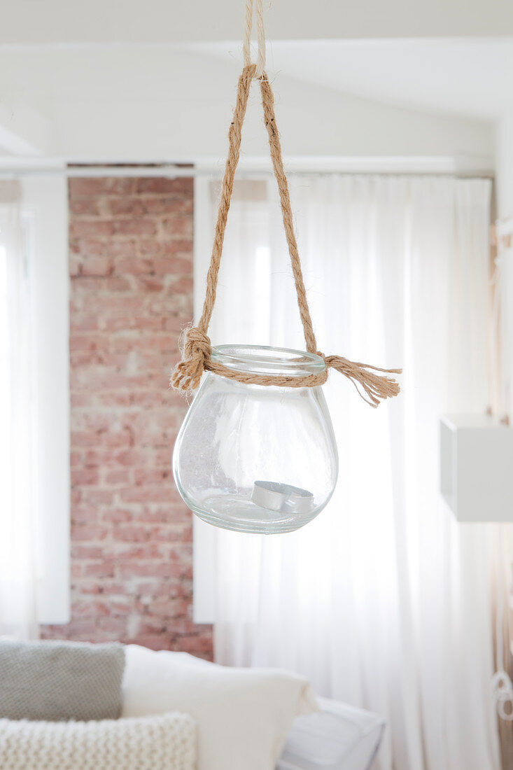 A lantern hung on a rope in a bright room with a brick wall