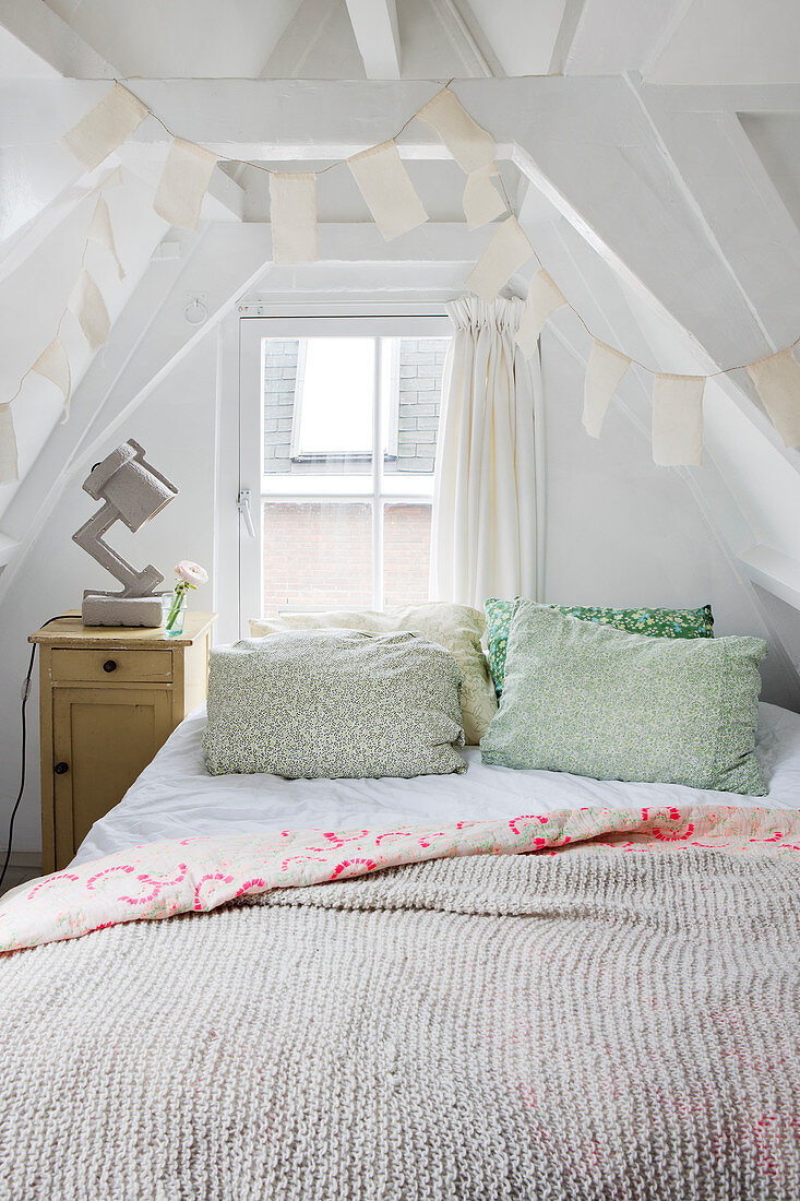 Scatter cushions on bed in converted attic with exposed wooden roof structure