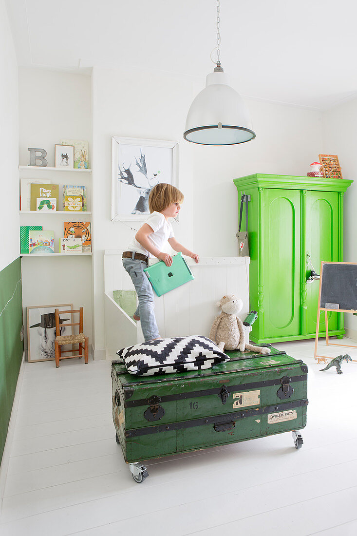 Boy stood on bed in white bedroom with green vintage furniture