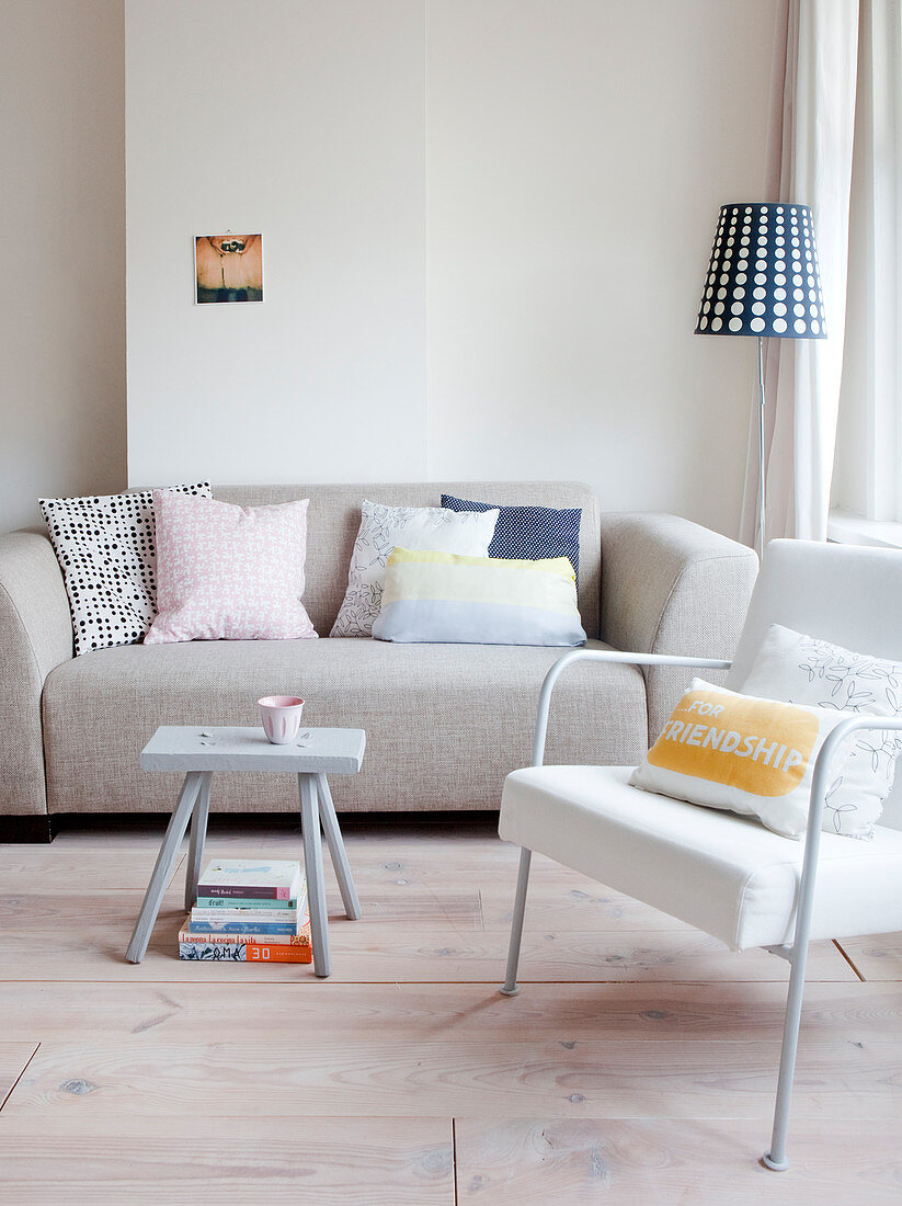 Scatter cushions on pale grey sofa, armchair and stool used as small table in living room