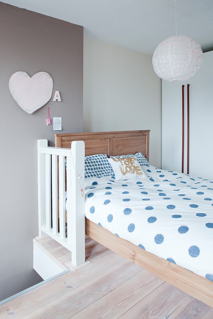 Holzbett mit blau gepunkteter Bettwäsche, darüber Hängelampe mit Papierschirm