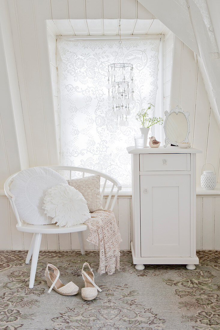 White cupboard and chair with pillows in front of the window in the attic room
