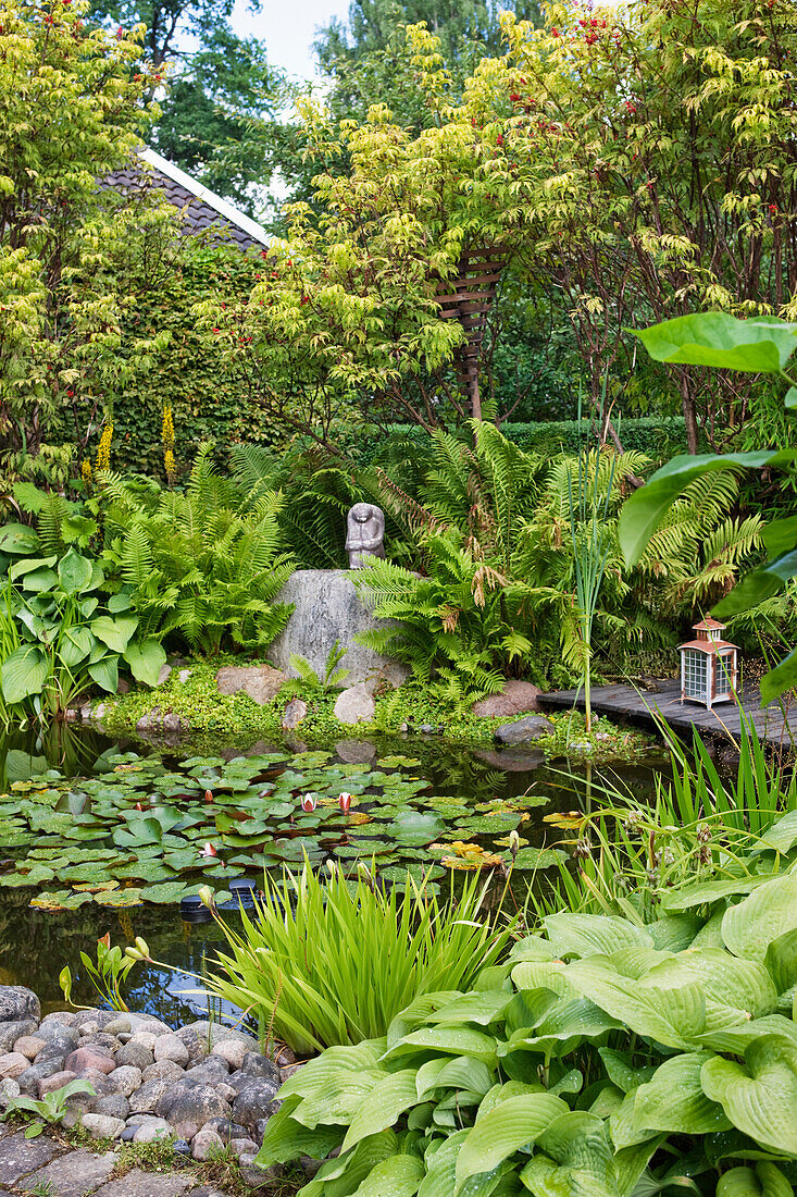 Garden pond with water lilies, wooden footbridge. and stone sculpture