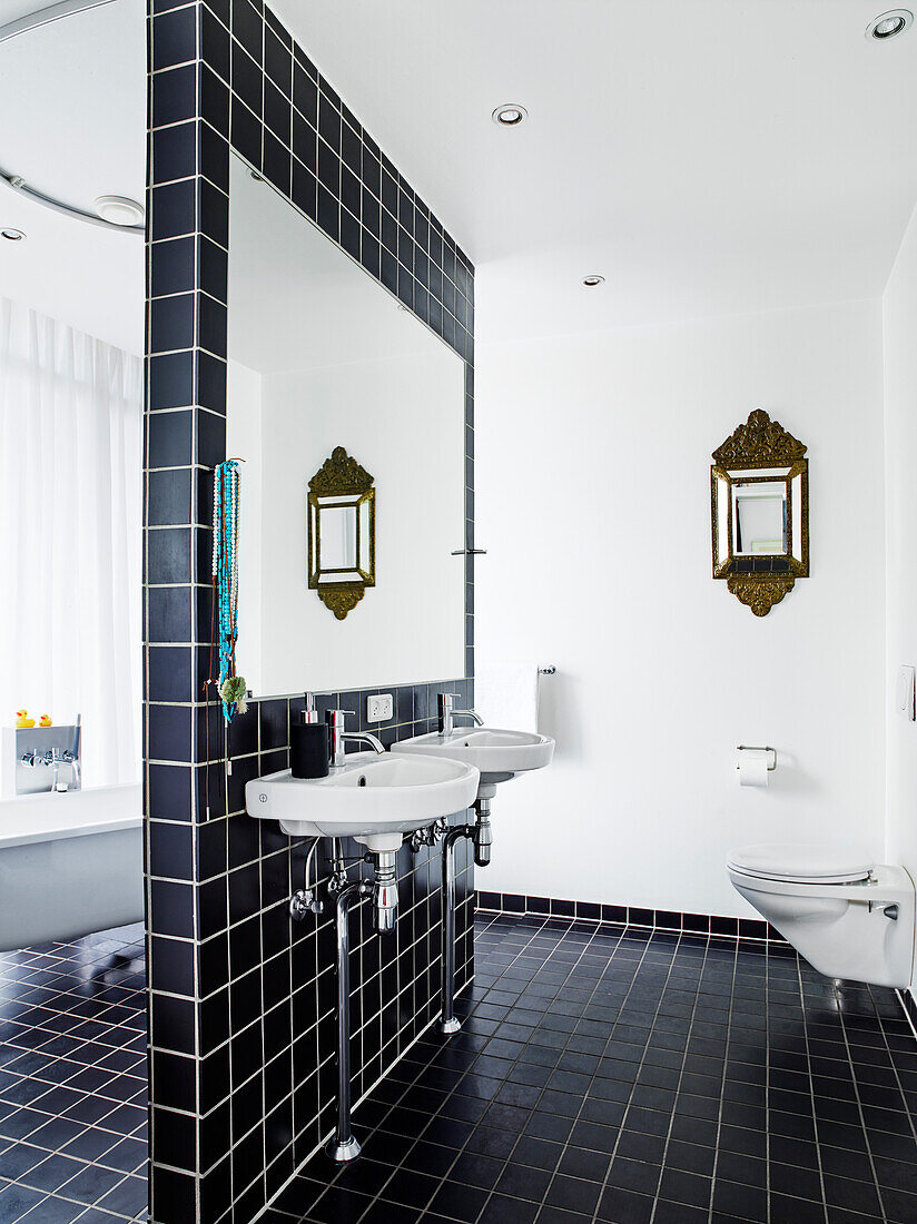 Waschbecken und Spiegel an Trennwand mit schwarzen Fliesen