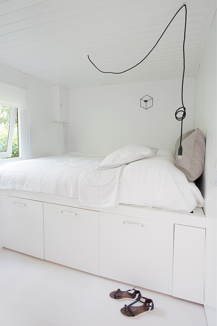 Weißes Bett mit Schubfächern darunter in weißem Schlafzimmer