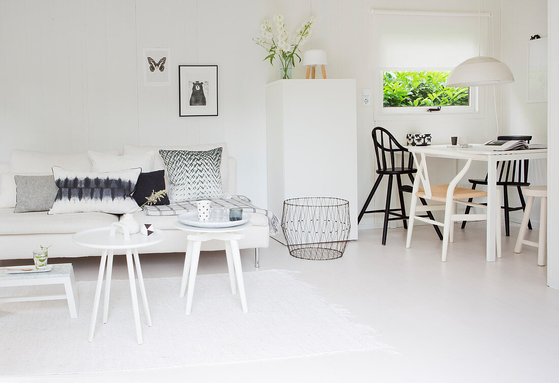 Weiße Couch mit Beistelltischen und Essbereich mit verschiedenen Stühlen in weißem, offenem Wohnraum