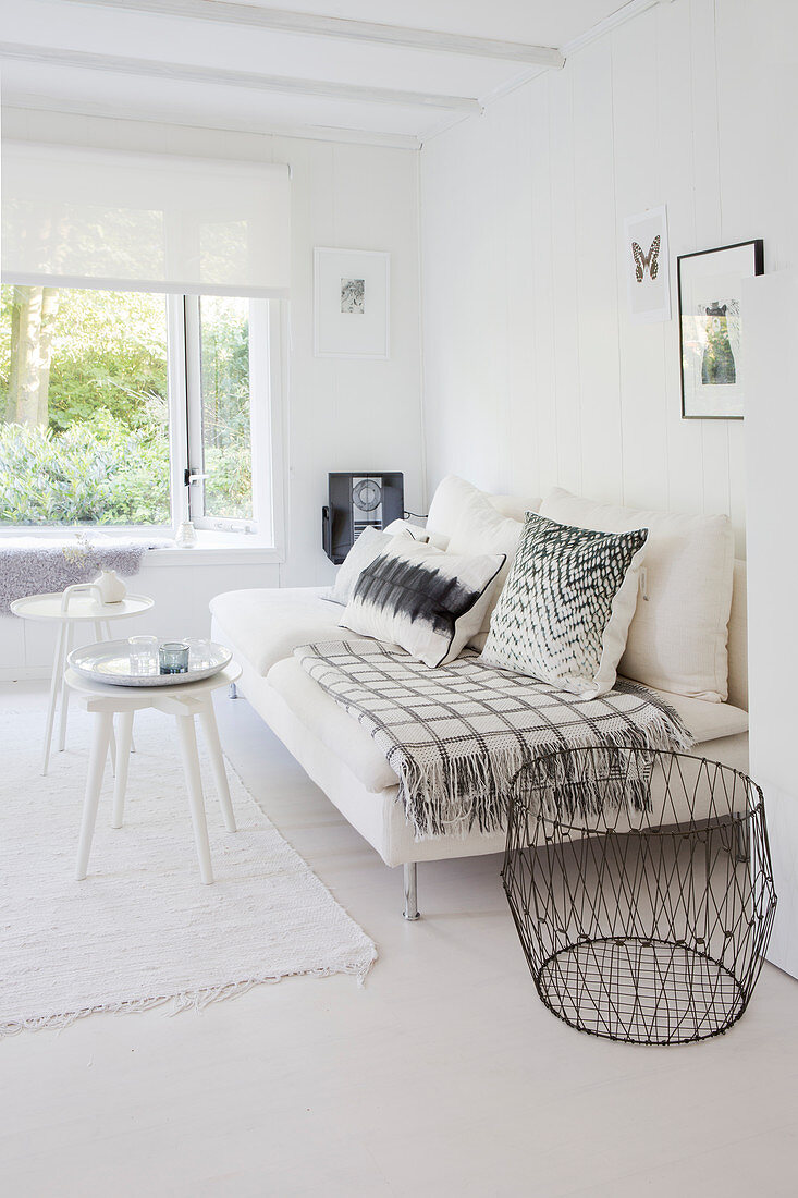 Weiße Couch mit Kissen, Beistelltische und Metallkorb in weißem Wohnzimmer