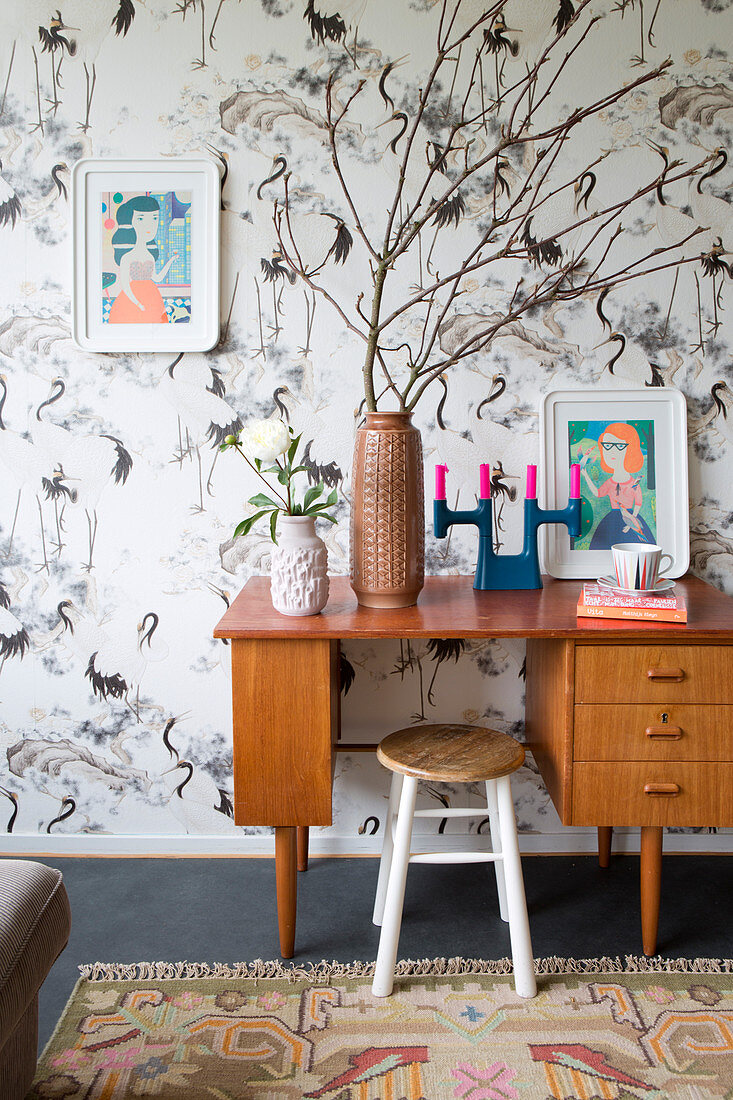 Retro desk and stool against bird-patterned wallpaper
