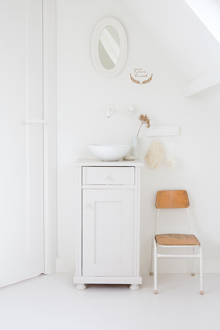 Waschschüssel auf weißem Unterschrank, daneben Stuhl