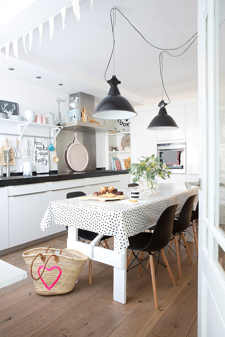 Esstisch mit schwarz-weiß gepunkteter Tischdecke und schwarze Klassikerstühle in offener Küche